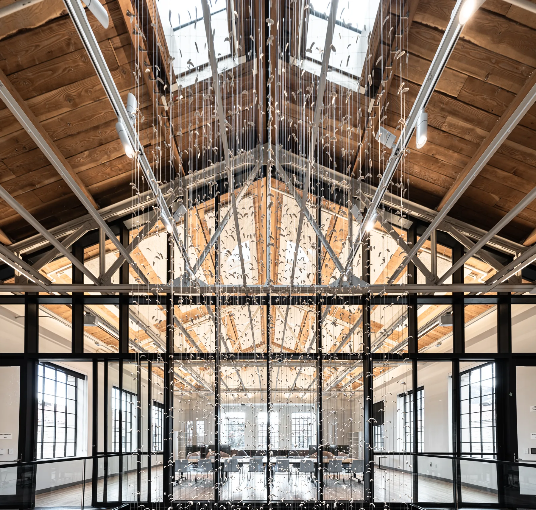 Hellems Hall atrium with exposed timber trusses, glass wall, and suspended art, University of Colorado Boulder