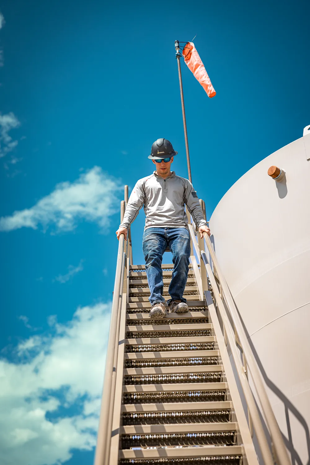 Worker descending a storage tank ladder against blue sky
