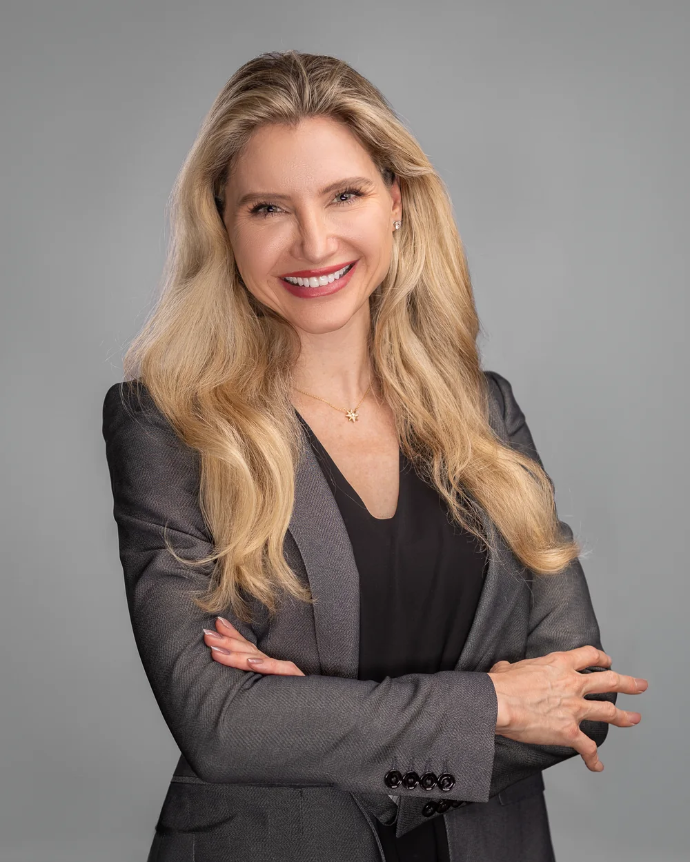 Executive portrait in a charcoal blazer, arms crossed, on a gray studio backdrop