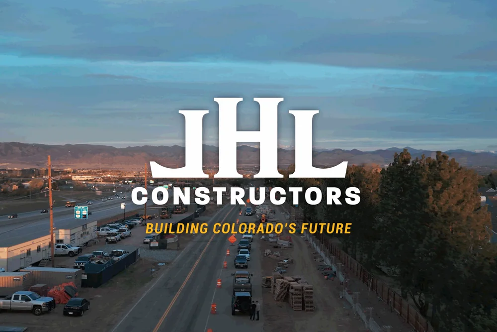JHL Constructors—Building Colorado’s Future—over a drone view of an active highway-side jobsite at dusk