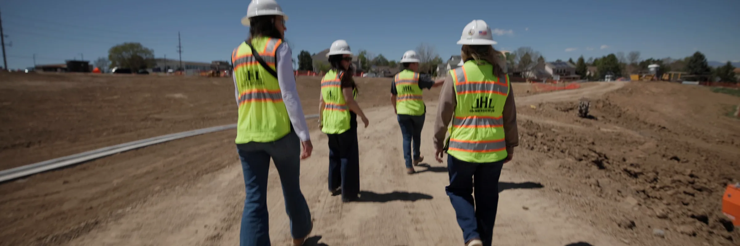 Four JHL team members in hi-vis vests walking a graded site