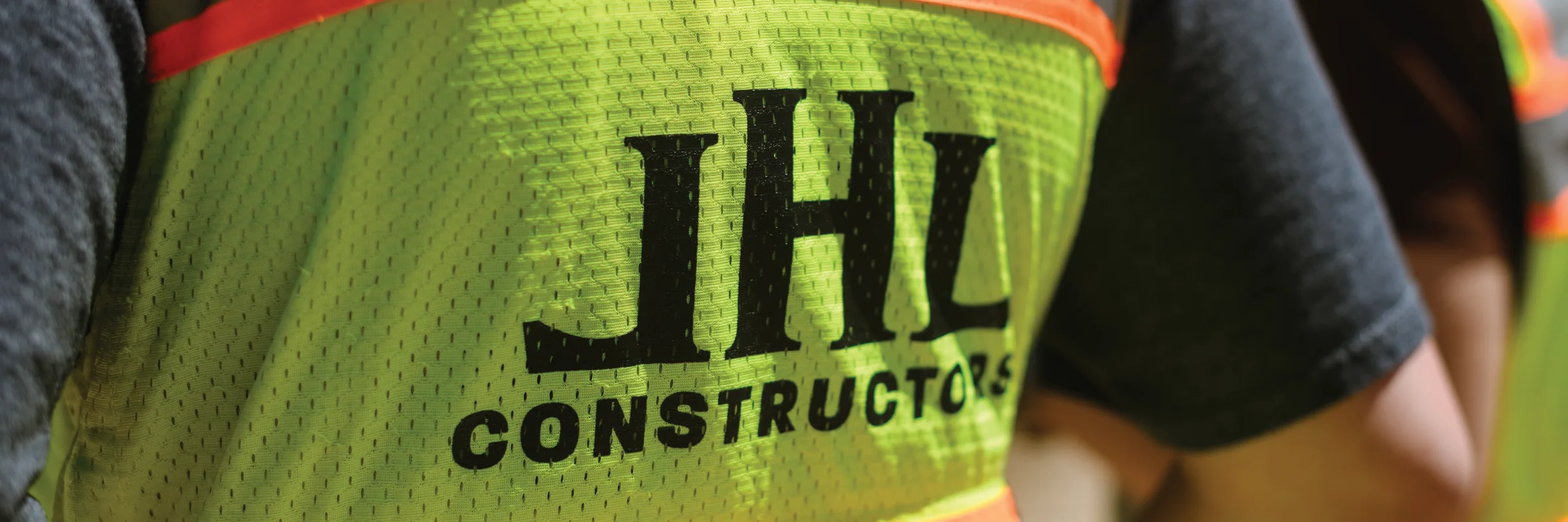 The JHL Constructors logo on the back of a hi-vis safety vest, close up on site